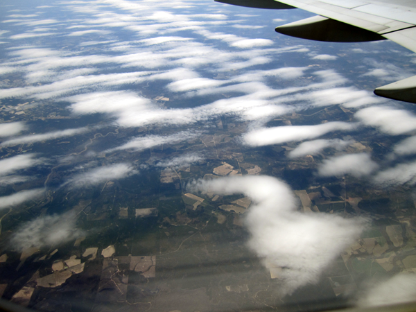 Green trees and fields are visible through the layer of whispy white clouds